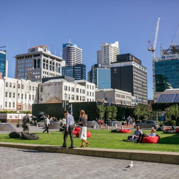 People walking through and sitting in Britomart's Takutai Square in Auckland's city centre, with cranes visible in the background. Image: Sacha Stejko.