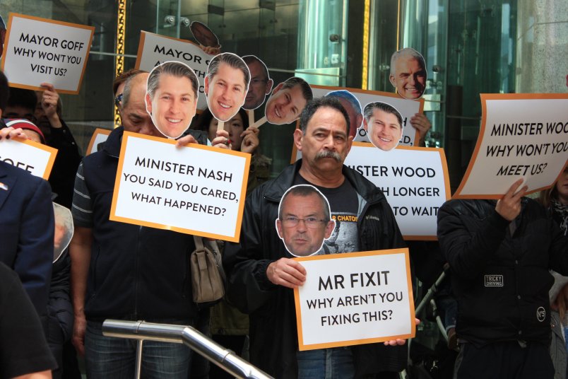 Business owners standing in front of Auckland Council headquarters with signs calling on decision makers for answers about financial support