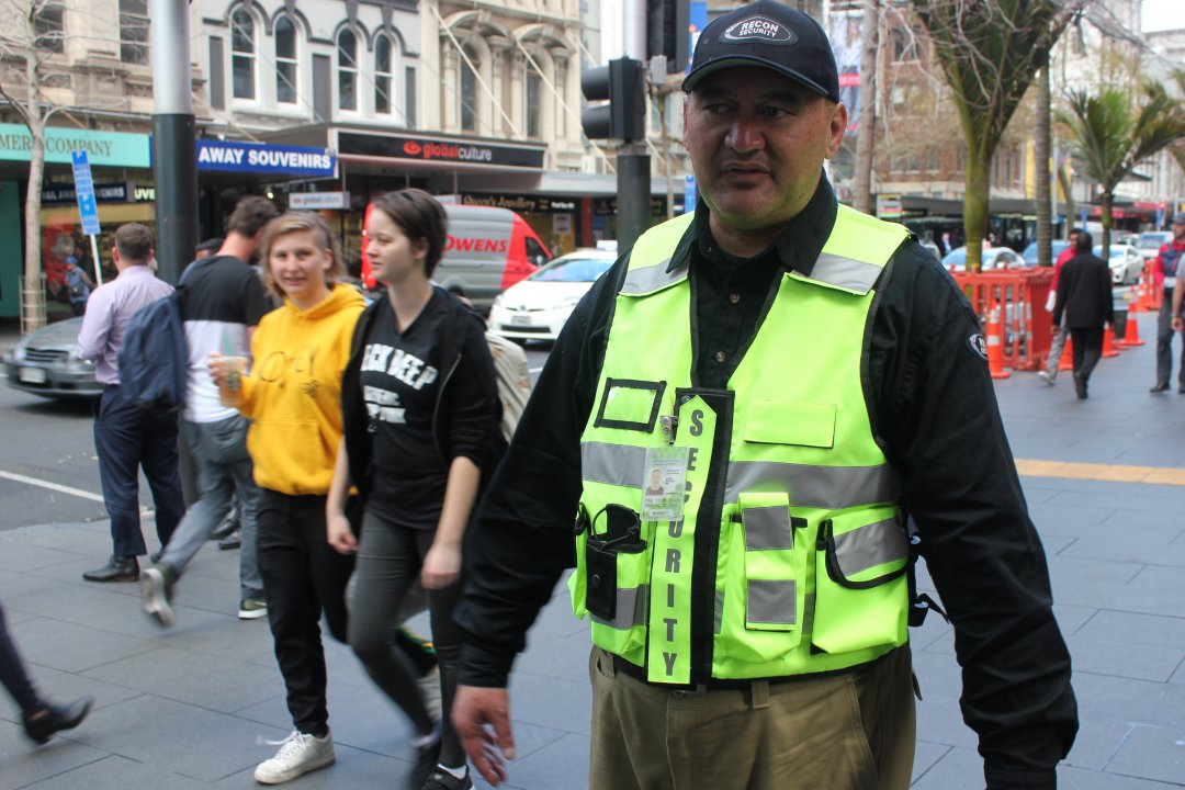 CityWatch team member JR John on Queen Street in Auckland City Centre among pedestrians, retail, green spaces, tourists, heritage buildings, 